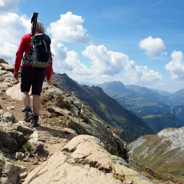 Randonneur sac au dos sur un sentier rocheux du Tour du Mont-Blanc, face aux vallées