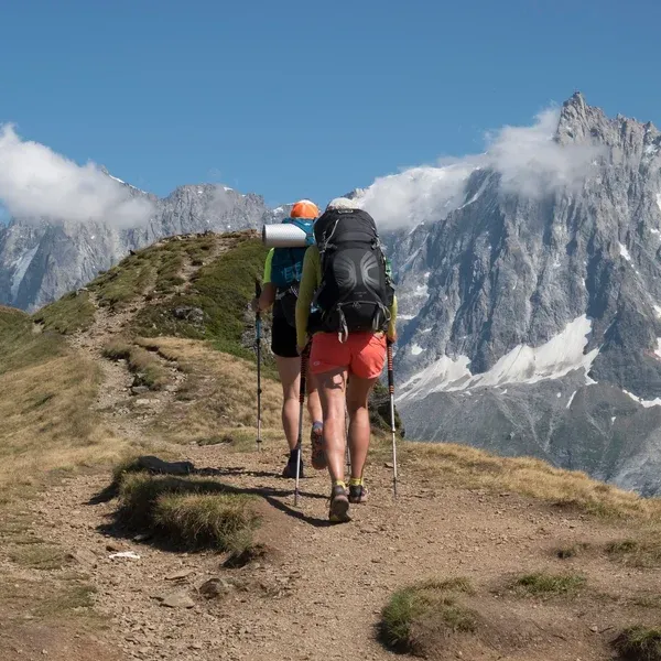 Deux randonneurs avec sacs à dos sur le sentier du Tour du Mont Blanc face au massif rocheux enneigé